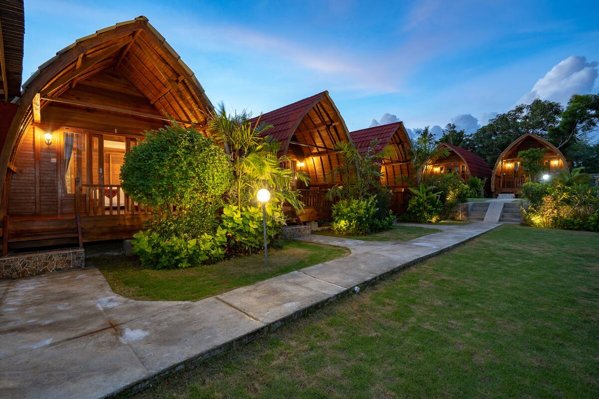 A row of wooden cabins with pitched roofs, each with a porch and a light fixture.