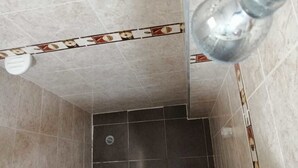 A bathroom with beige and dark gray tiles, a visible drain, and a light fixture. - Apartamentos Nayibe (Cartagena)
