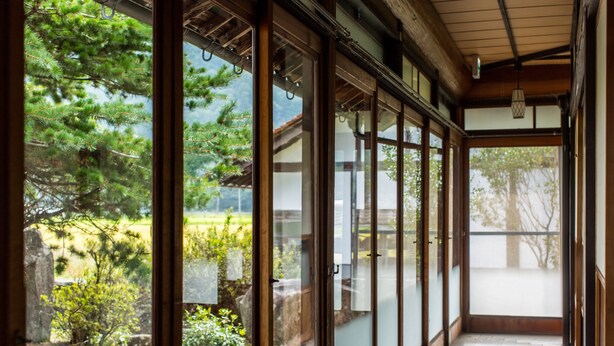 Una habitación japonesa tradicional con puertas correderas, suelo de madera y vistas a un jardín con árboles y un estanque.