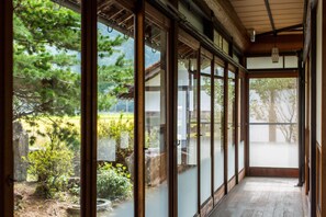 Een traditionele Japanse kamer met glijdende deuren, een houten vloer en uitzicht op een tuin met bomen en een vijver.