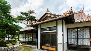Un edificio tradicional japonés con techo de tejas, puertas de madera y un sendero de piedra que lleva a la entrada.