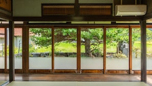 Una habitación japonesa tradicional con suelo de tatami, puertas correderas y vistas a un jardín exuberante.