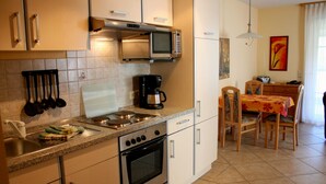 A compact kitchen with a microwave, stove, and coffee maker. There is a dining area with a table and chairs. - Apartment 12 - apartment / apartment in Binz (Binz)