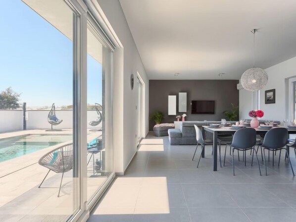 Una sala de estar moderna con piscina, comedor y televisor montado en la pared.