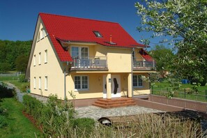 Uma casa de dois andares com telhado vermelho, uma varanda e um pequeno jardim.
