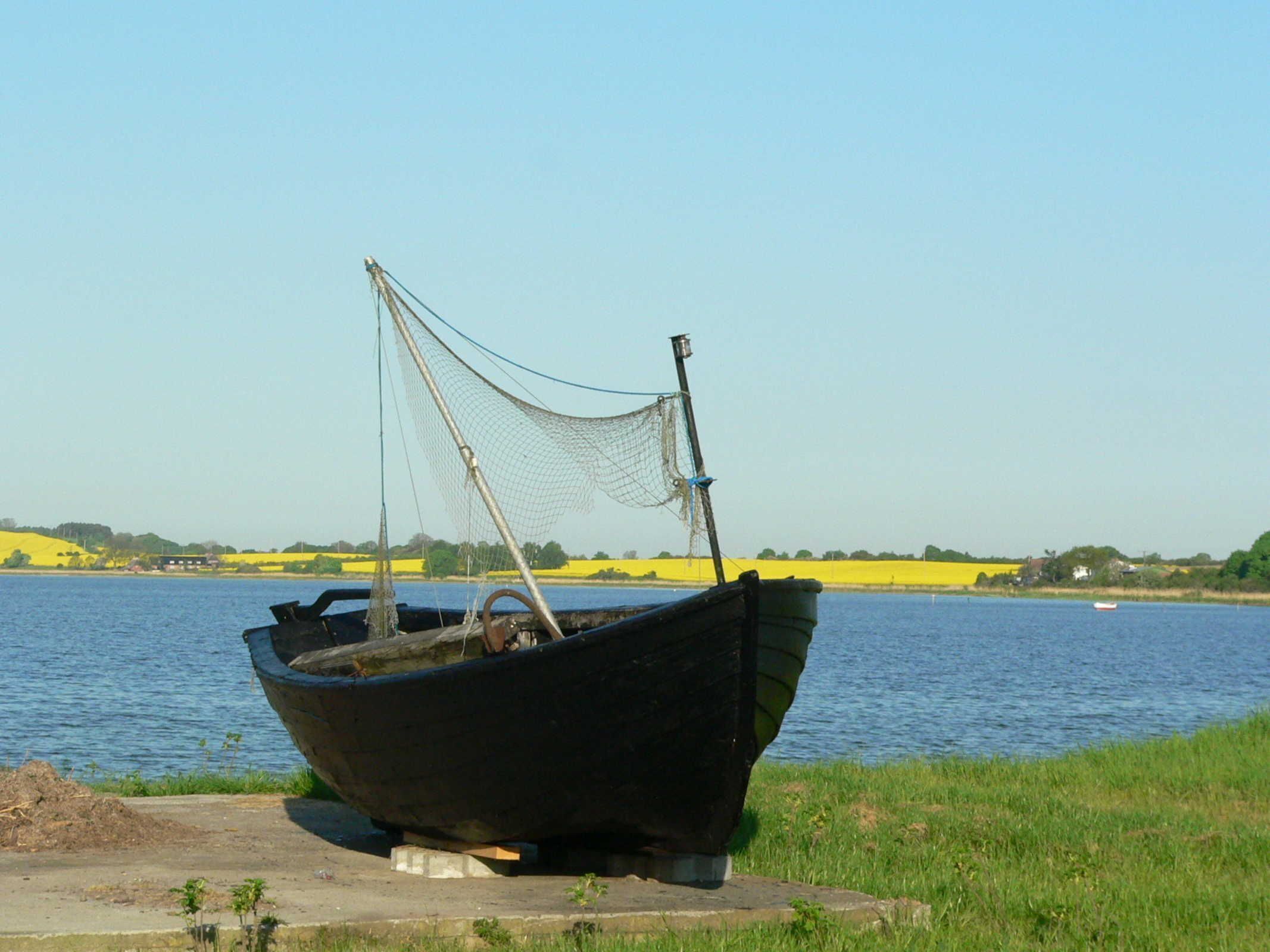 Un bote antiguo con una red sobre una plataforma de concreto a orillas de un río tranquilo.
