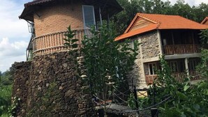 Un edificio de piedra de dos pisos con un balcón, rodeado de vegetación y un cielo despejado.