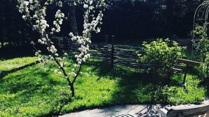 A patio area with two wooden rocking chairs, a small tree with white blossoms, and a metal fence in the background.