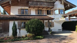 A traditional chalet with a wooden balcony, a tiled roof, and a garden area with a small pond.