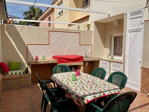 Eine Terrasse im Freien mit Tisch und Stühlen, einem Grill und einer kleinen Sitzecke.