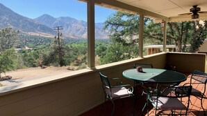 Un porche cubierto con una mesa y sillas, con vistas a un paisaje montañoso.