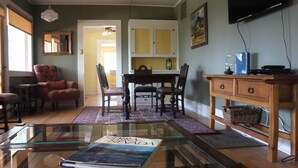 Una sala de estar con una mesa de centro de vidrio, un sillón rojo, una mesa de comedor con sillas y un mueble de madera.