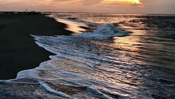 En strand med vågor i solnedgången.