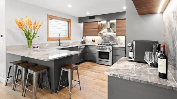 A modern kitchen with a large island, wooden bar stools, a built-in oven, and a wine bottle on the counter. - Luxury Mountainside Retreat at Silver Star — 3 King En-Suites (Park City)