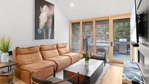 A modern living room with a brown leather sofa, a glass coffee table, and a TV mounted on the wall. - Luxury Mountainside Retreat at Silver Star — 3 King En-Suites (Park City)
