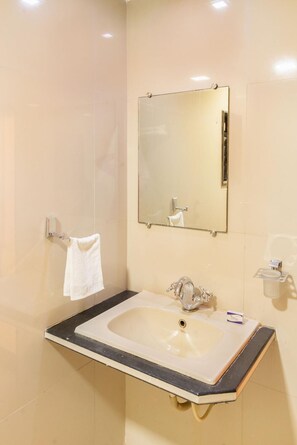 A bathroom with a sink, mirror, and towel rack. - Hotel Sheetal Plaza (Surat)
