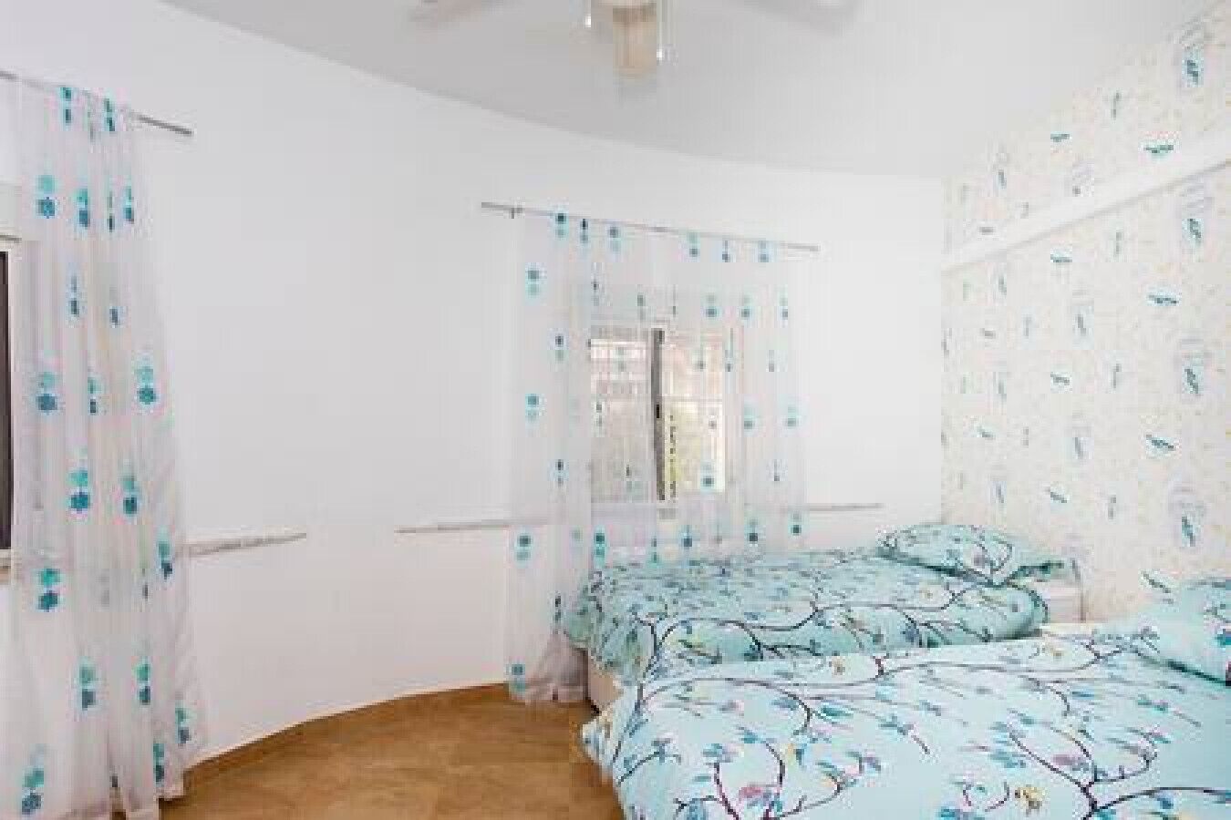 A bedroom with two beds, a window with a curtain, and a ceiling fan.