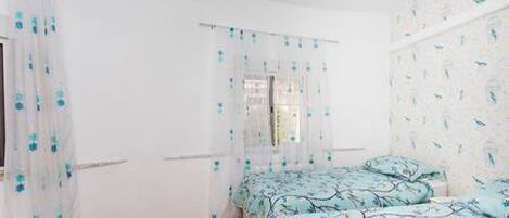 A bedroom with two beds, a window with a curtain, and a ceiling fan.