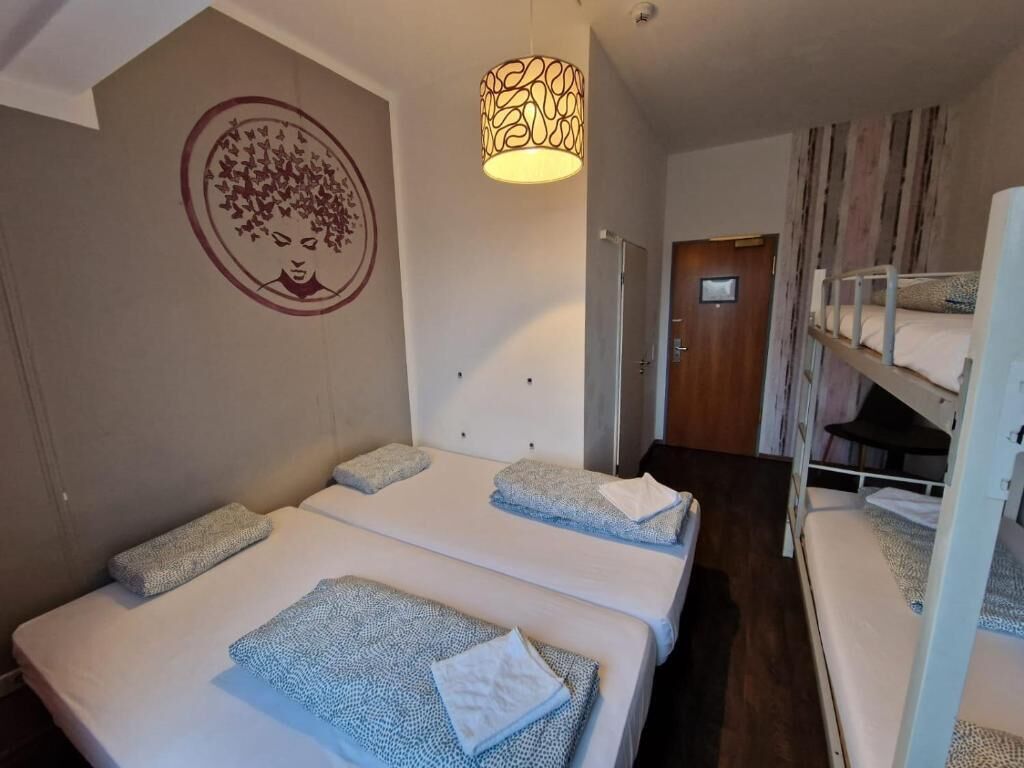 A hotel room with two single beds, a bunk bed, a wooden door, and a wall with a circular design.