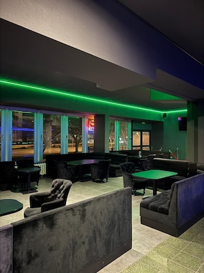 A modern lounge area with seating and tables, large windows with views, and green ambient lighting. - Ootel.com (Berlin)