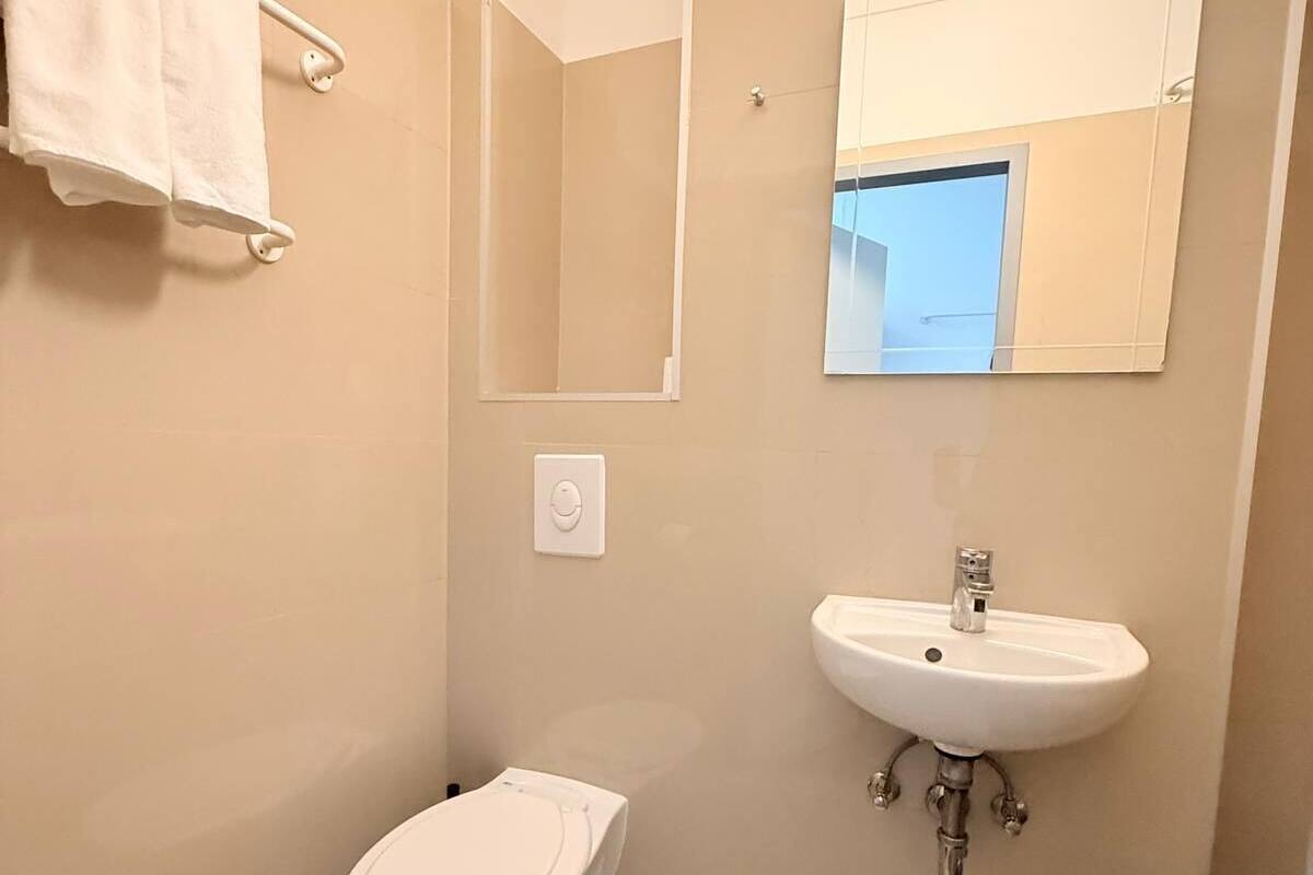 A bathroom with a toilet, sink, mirror, and towel rack.