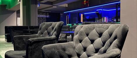 A modern lounge area with tufted chairs and a bar area with neon lighting.