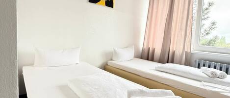 Una camera d'albergo con due letti, una finestra con tende, un termosifone e un quadro appeso al muro.
