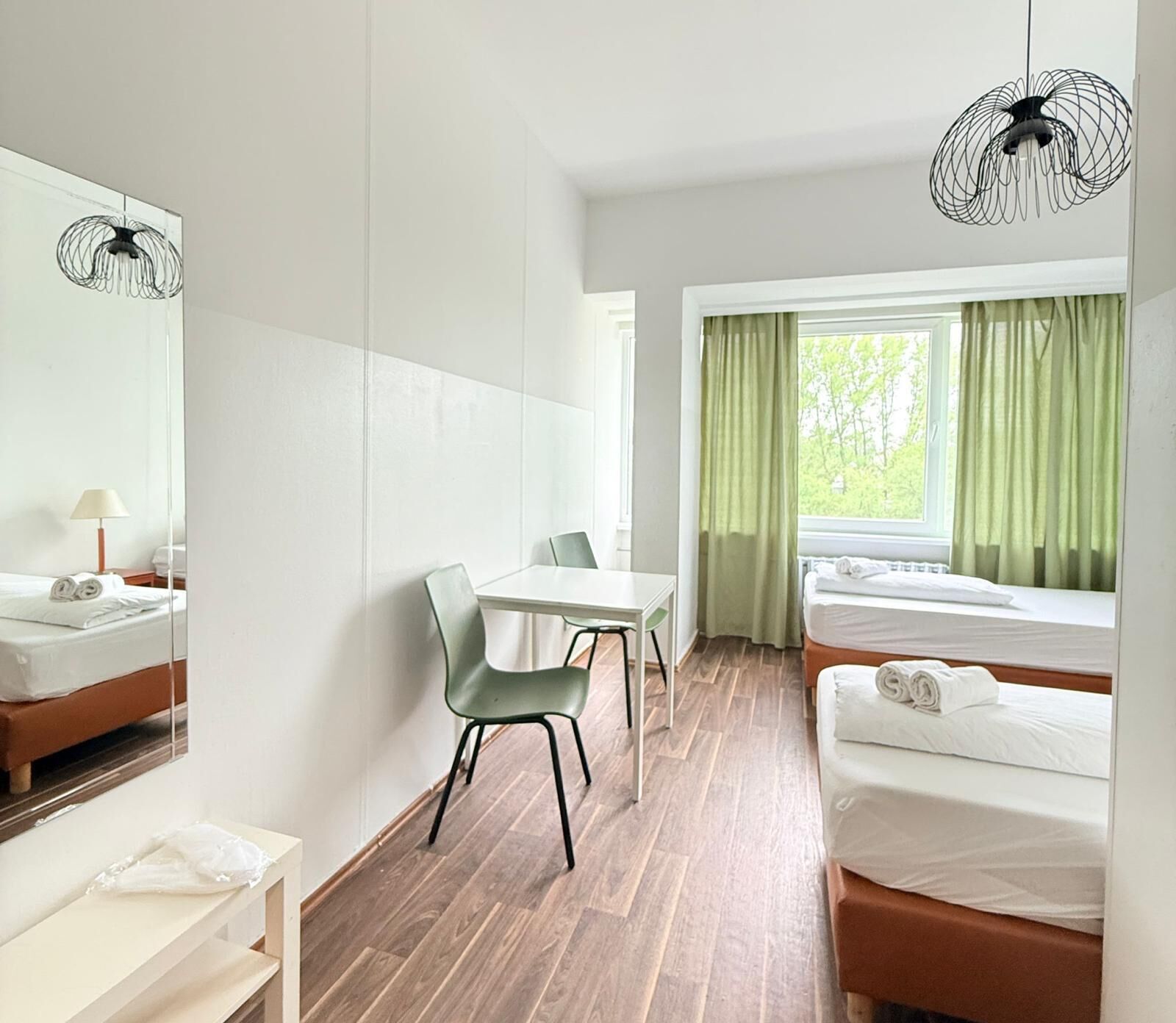 Une chambre d’hôtel avec un lit, un bureau, une chaise, un miroir et une fenêtre avec des rideaux.