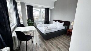 Habitación de hotel con cama, escritorio, silla, radiador y ventana con cortinas.