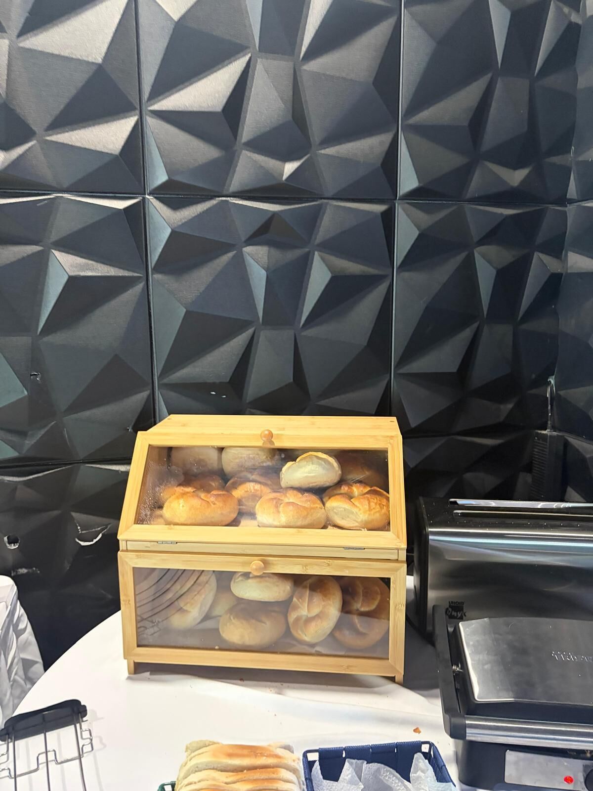 A buffet setup with a wooden display case containing baked goods, a black appliance, and a white tablecloth.