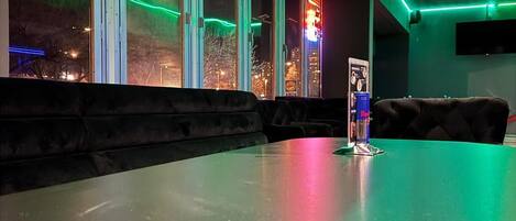 A bar area with a long counter, cushioned seating, and large windows with city views.