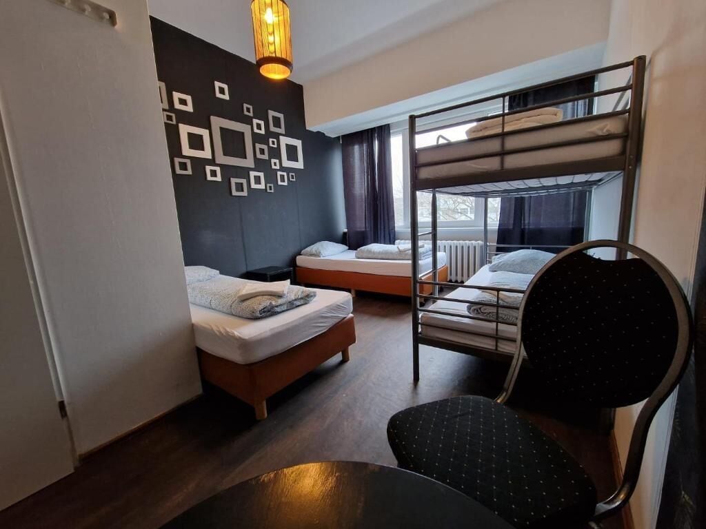 A compact hotel room with a bunk bed, a single bed, a chair, and a table.