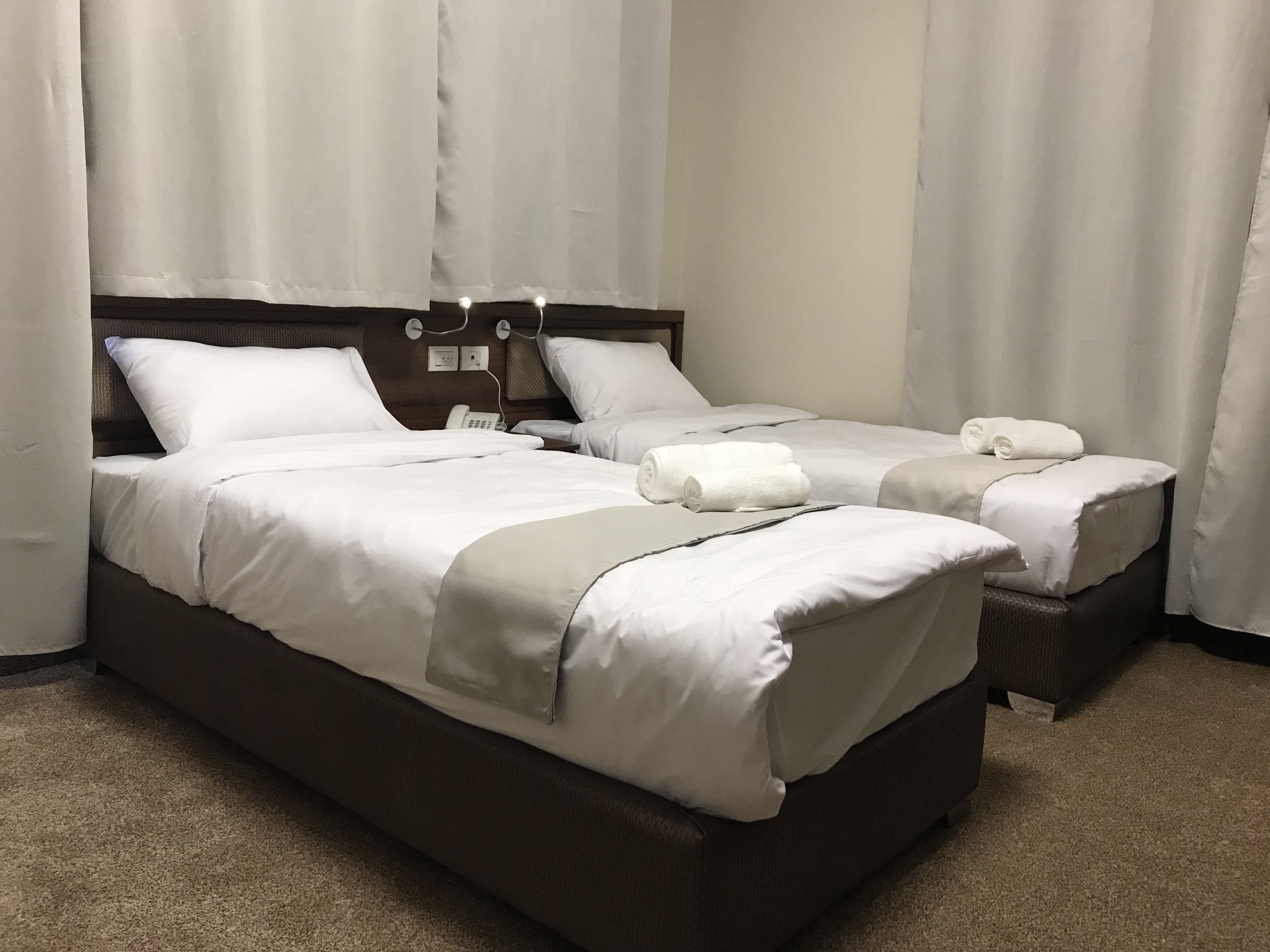 A double bed with white linens and two rolled towels, a bedside telephone, and a nightstand.