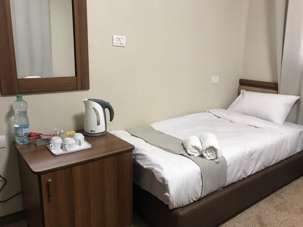 A hotel room with a bed, a wooden nightstand, a kettle, a bottle of water, and a tray with cups and a teapot. - Eli Guest House (Bayt Sahur)