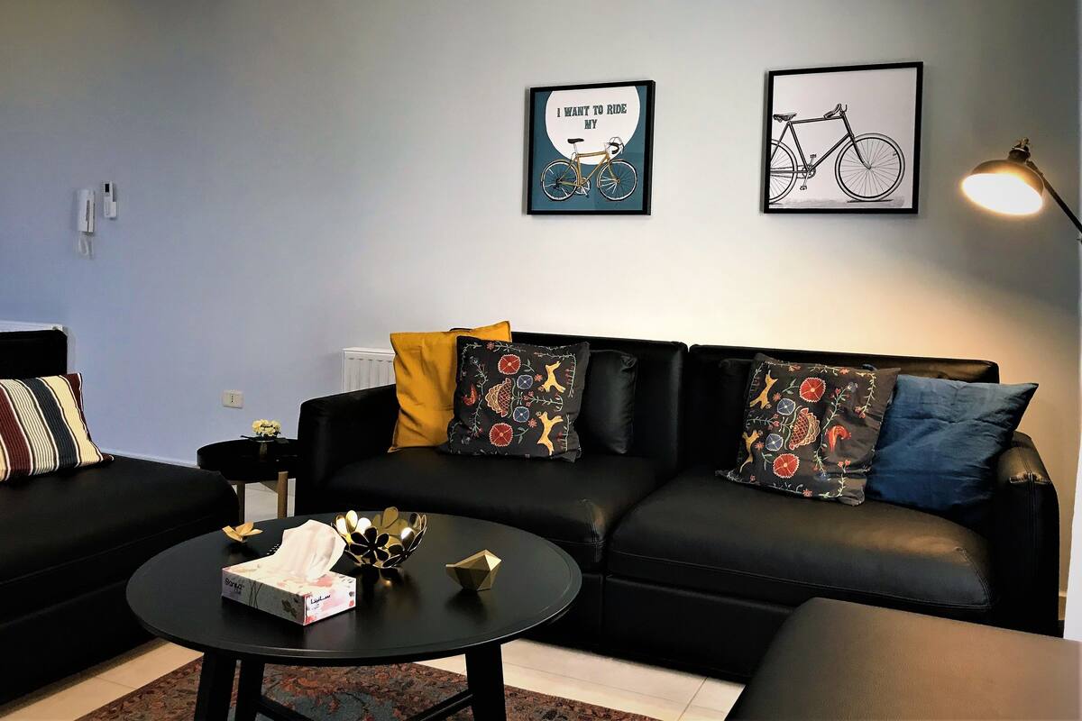 A modern living room with a black leather sofa, a round coffee table, and two framed pictures on the wall.