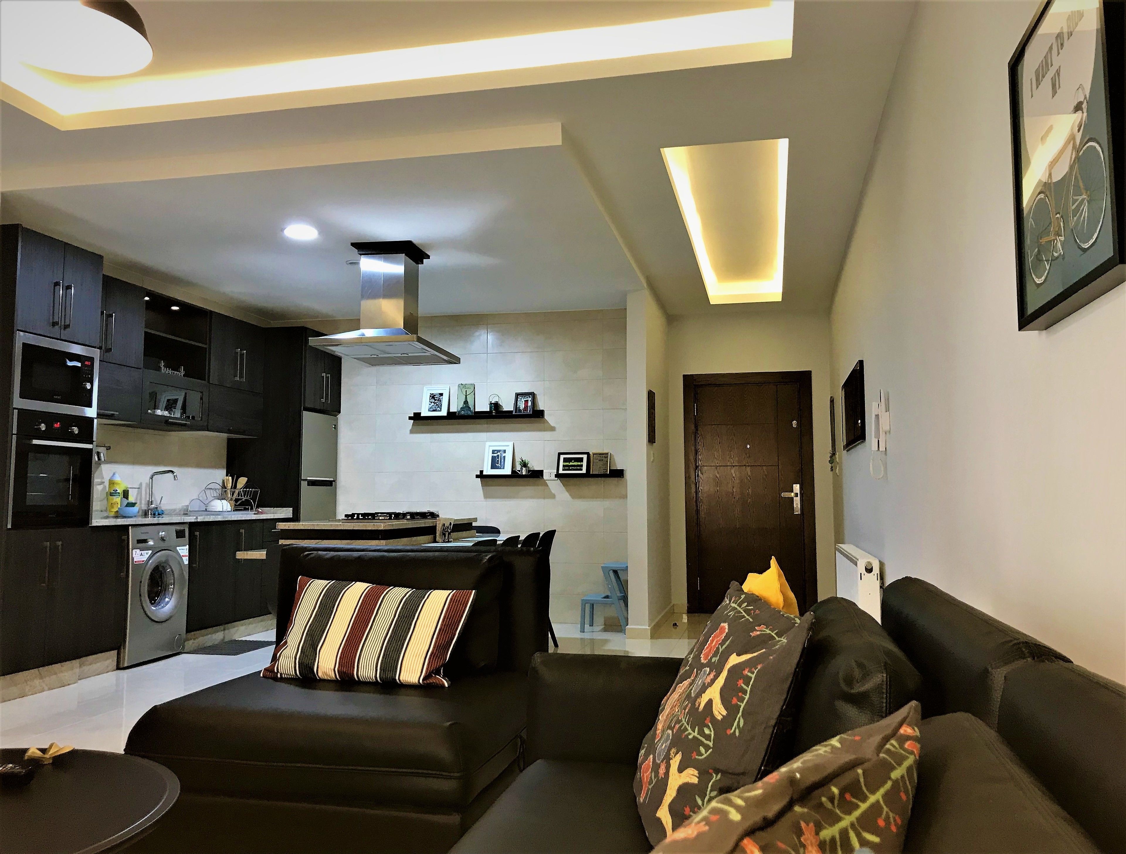 A modern living room with a sofa, a coffee table, and a kitchen area with dark cabinets and appliances.