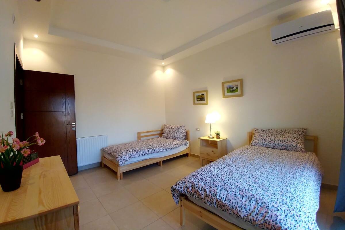 A small, well-lit bedroom with two single beds, a wooden desk, a mirror, and a radiator.