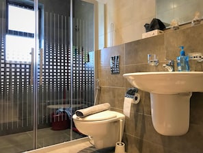 A modern bathroom with a glass shower enclosure, a toilet, and a sink with a mirror above. - Double Key by HR (Amman)