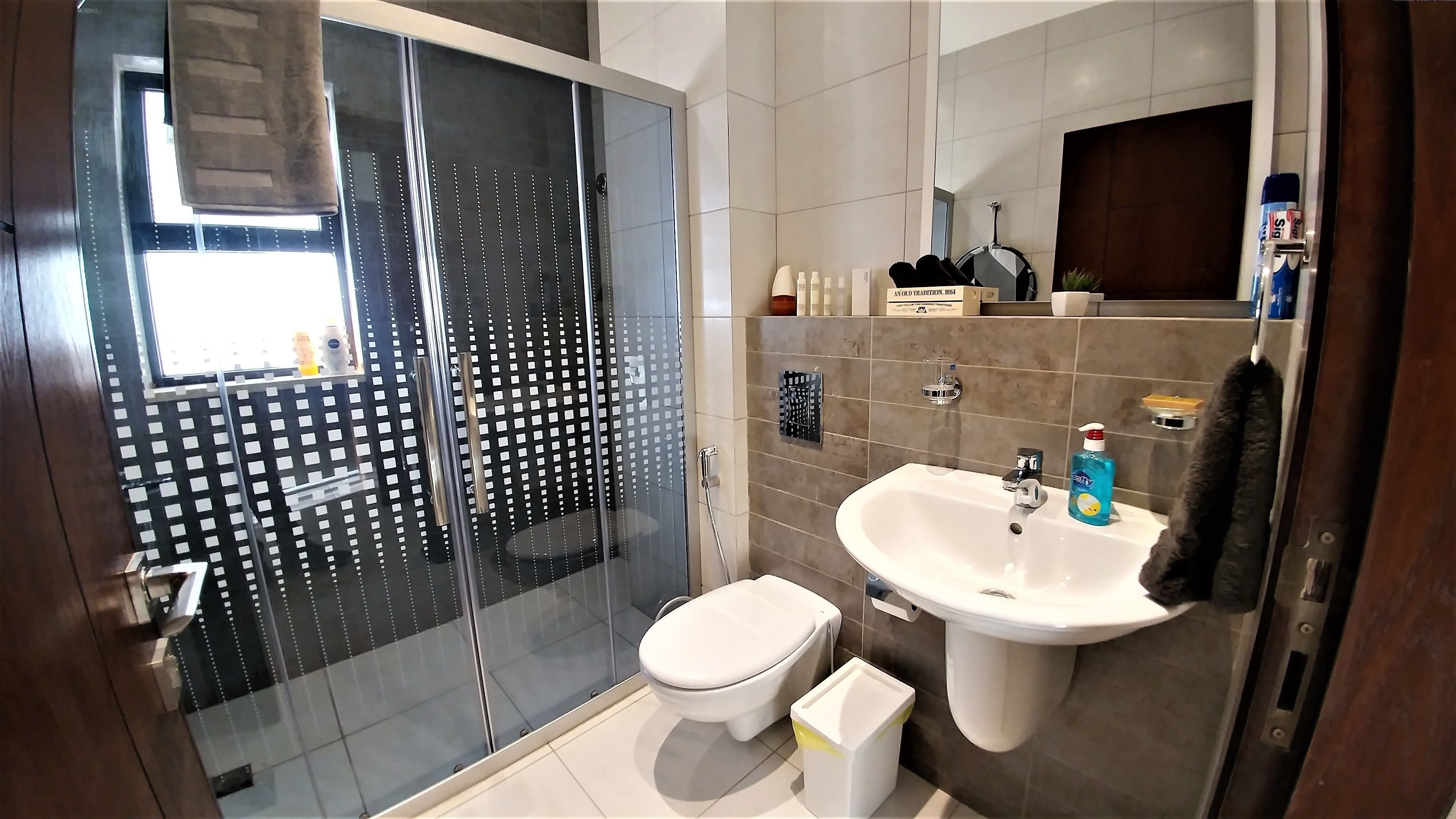 Een moderne badkamer met een douchecabine van glas, een wit toilet en een wastafel met een spiegel erboven.
