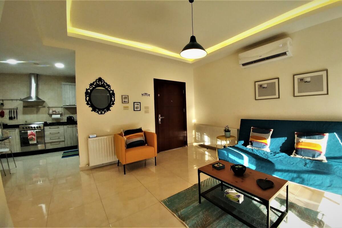 A modern living room with a sofa, coffee table, and a view of the kitchen.