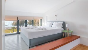 Une chambre moderne avec un grand lit, une vue sur la mer et une table de chevet verte avec une lampe.