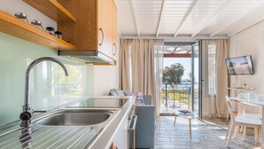 Une cuisine moderne dotée d’un  évier en acier inoxydable et de meubles en bois, un coin repas avec une table et des chaises, et une vue sur l’extérieur grâce à une porte vitrée.