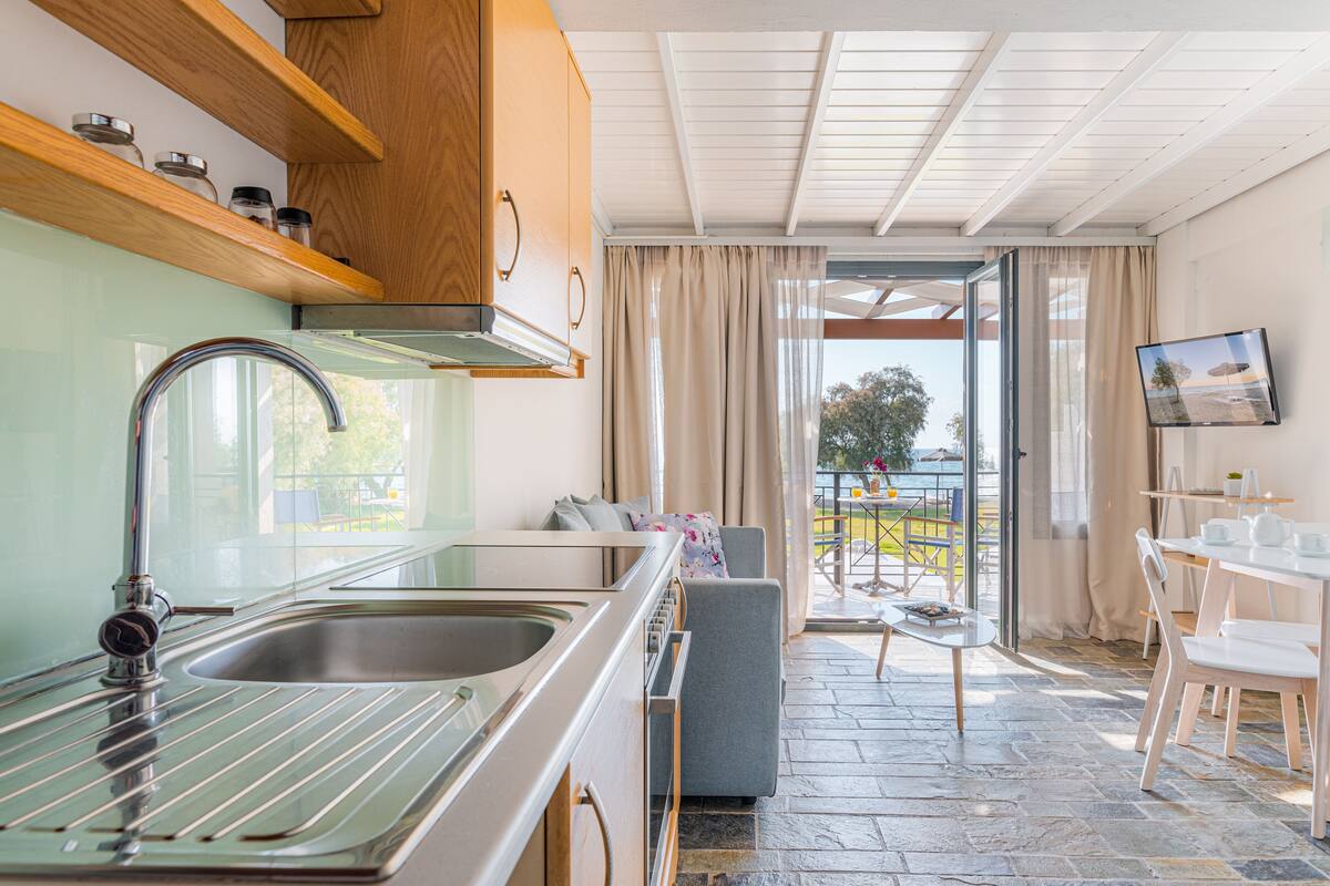 Una cocina moderna con un lavamanos de acero inoxidable y armarios de madera, un comedor con mesa y sillas, y vistas al exterior a través de un ventanal.