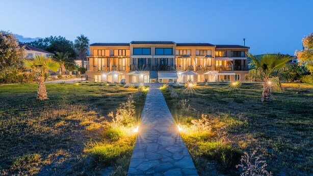 Un bâtiment moderne à deux étages, avec un chemin en pierre menant à l’entrée, entouré de pelouses bien entretenues et de palmiers.