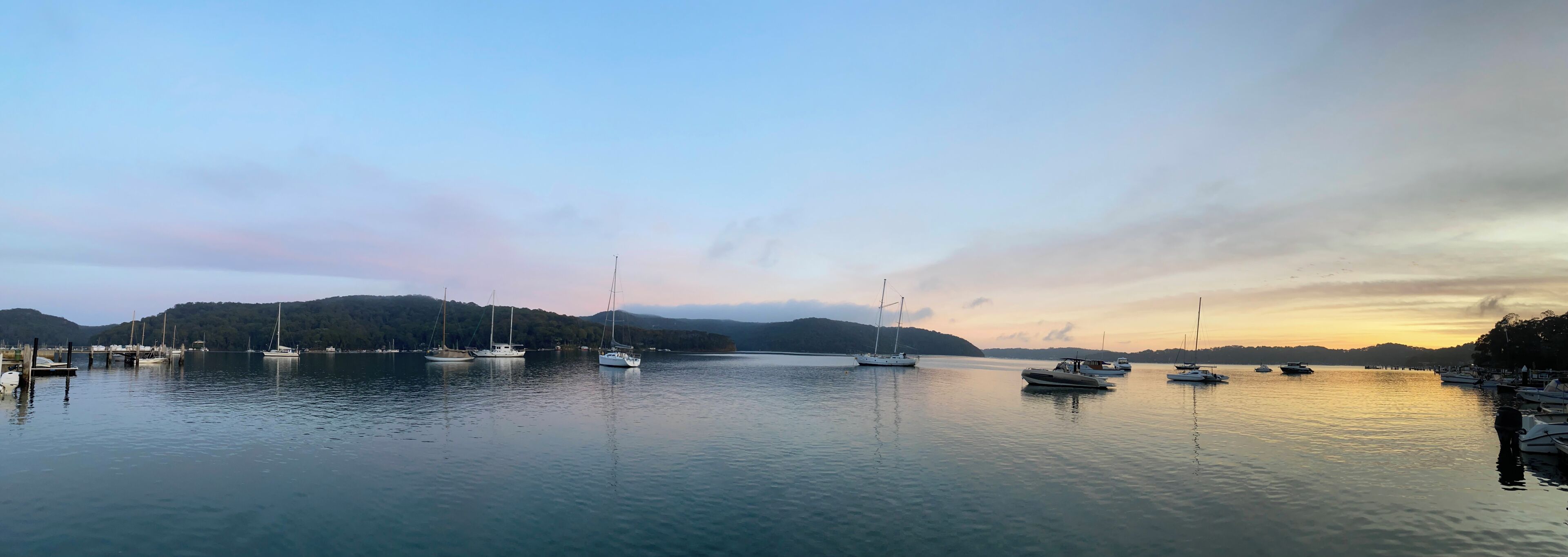 Un port de plaisance où sont amarrés plusieurs bateaux, avec une eau calme et un paysage vallonné en arrière-plan.