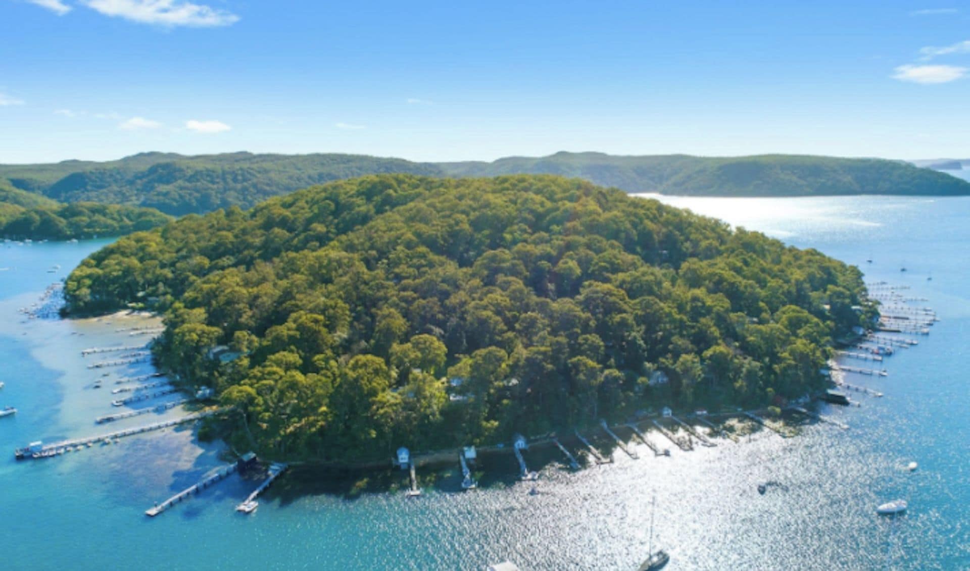 An aerial view of a lush, forested island surrounded by calm blue waters with boats anchored near the shore.