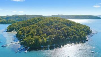 An aerial view of a lush, forested island surrounded by calm blue waters with boats anchored near the shore.
