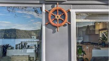 Une décoration murale sur le thème de la navigation, avec un gouvernail de navire, une porte vitrée donnant sur la mer et un aperçu d’un coin cuisine.