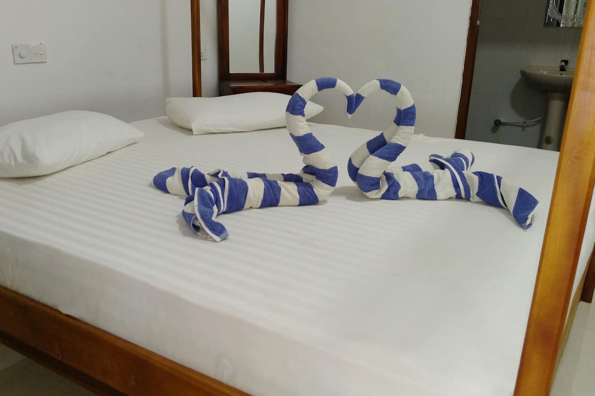 Een bed met witte lakens en kussens, een houten hoofdbord, en een badkamer is zichtbaar op de achtergrond.