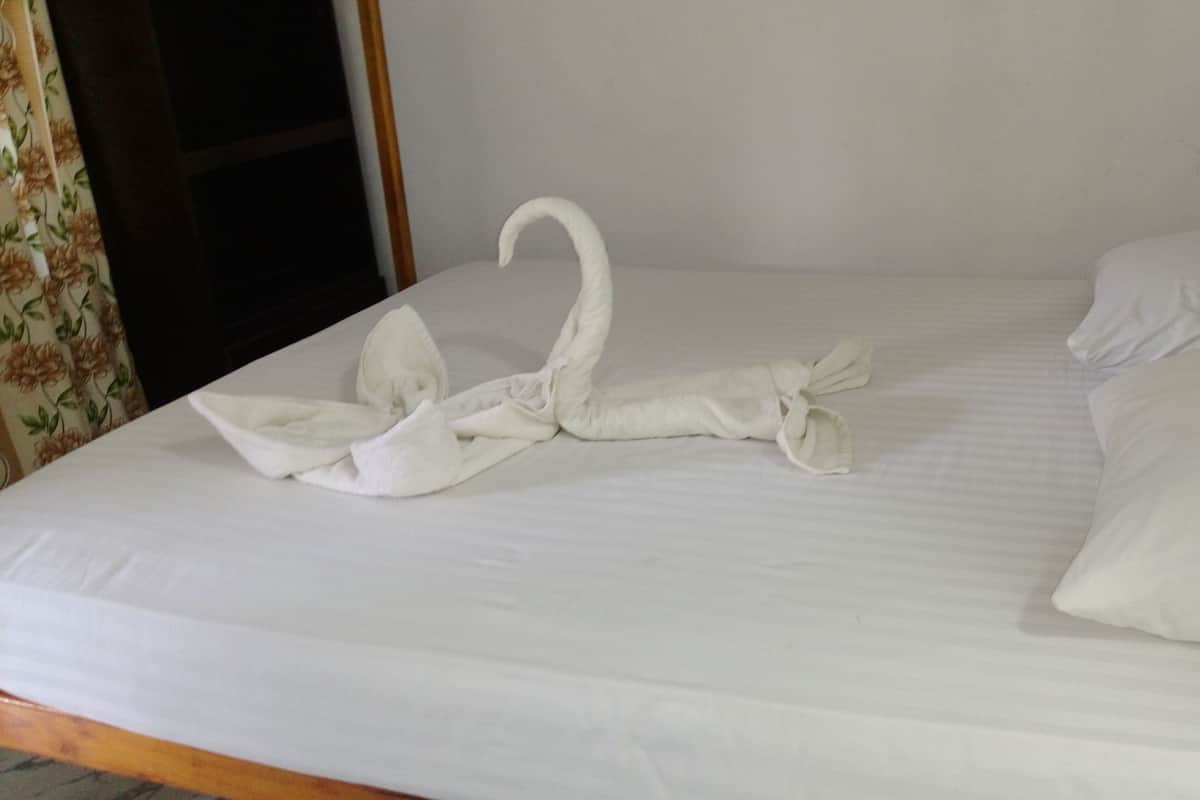 Een net opgemaakt bed met een handdoek gevouwen in de vorm van een zwaan.